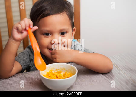 A cute young kid sitting at a table with an eager facial expression and spoon in hand, ready to start eating on his own. Stock Photo