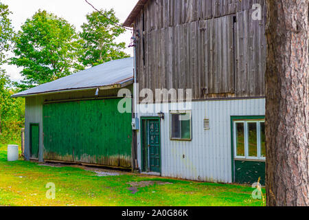 A small wooden barn has green and white siding and a green door. Stock Photo