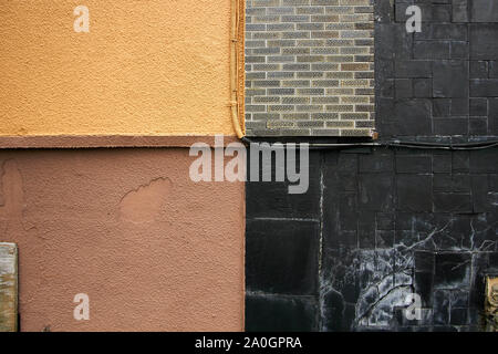 One wall made of four different patterns meeting in one corner. Brick, plaster, brown, yellow, black, gray. Stock Photo