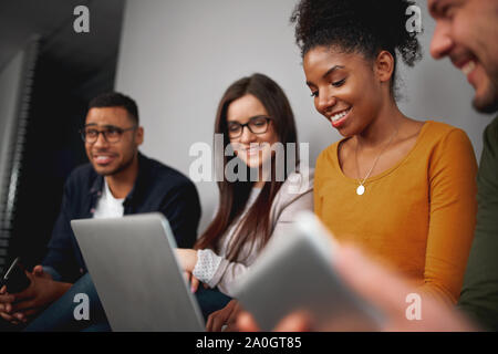 Group of multiethnic friends sitting in line looking at laptop, smiling and reading funny news in social network Stock Photo