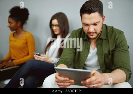Unemployed young man sit in queue with other applicants wait for company work interview using digital tablet Stock Photo