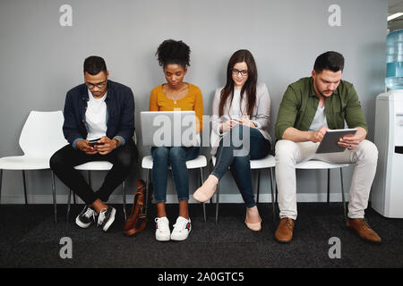 Diverse work candidates sitting in queue in office for job interview using modern gadgets preparing for recruiting process Stock Photo