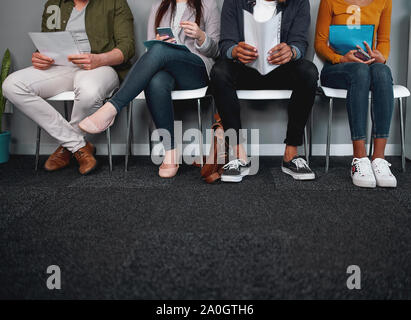 Low section of job applicants waiting in corridor preparing for recruiting process - photo of diverse feet sitting in a row waiting for job interview Stock Photo
