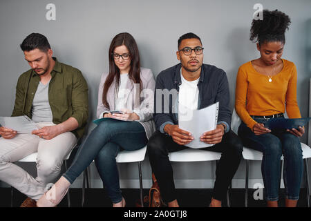 Group of multiracial young candidates waiting for interview sitting on chair holding their resumes  Stock Photo
