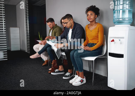 Young woman looking confident while sitting with a diverse group of job applicants in an office waiting for interviews Stock Photo