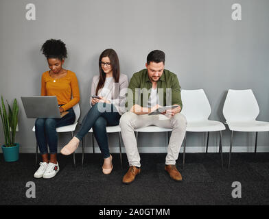Young multiethnic people sitting on chair chatting and browsing online in smartphones, digital tablet and laptop preparing for interview Stock Photo
