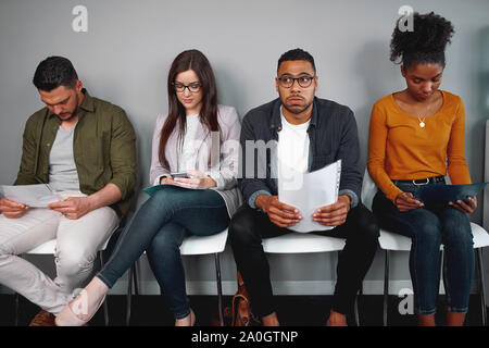 Worried and stressed man holding his resume sitting with other candidates waiting for the job interview in office - diverse young group of candidates Stock Photo