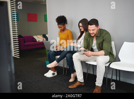 Group of multicultural young people sitting in row on chair for job interview using laptop, digital tablet and smartphone Stock Photo