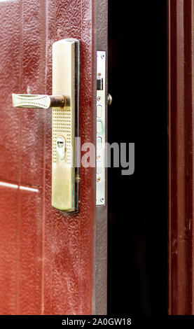 Open metal door with a shiny lock and handle. Close-up, selective focus, brown paint on the door Stock Photo