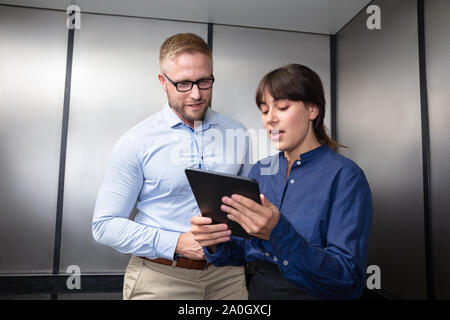 Portrait Of A Businessman And Businesswoman Standing In Elevator Discussing The Project On Digital Tablet Stock Photo