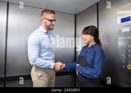 Successful Young Business Colleague In Formalwear Smiling And Shaking Each Other's Hand In The Elevator Stock Photo