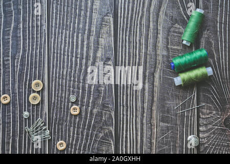 Sewing accessories on dark wooden background. Green sewing threads, needles, buttons and pins. top view, flatlay Stock Photo