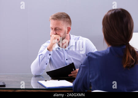 Young Businesswoman Looking At Worried Thoughtful Businessman Sitting At Interview In Office Stock Photo