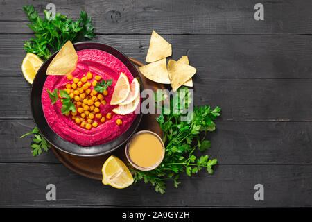 Tasty and healthy food concept. Fresh beetroot hummus in plate with chickpeas and pita bread on dark background top view Stock Photo