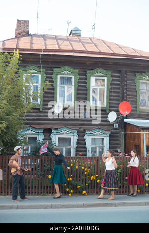 People standing on the street of russian village - a pretty woman in emerald skirt with handkerchief dancing by the music from balalaika Stock Photo