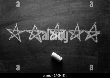 Five hand sketched white stars on a chalkboard or blackboard with piece of chalk below in a concept of grading for excellence Stock Photo