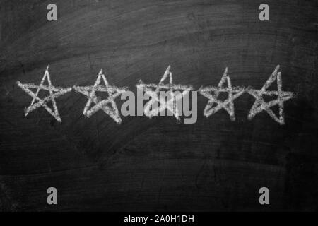 Five white chalk stars hand drawn on a blackboard in a row conceptual of a five star rating for excellence Stock Photo