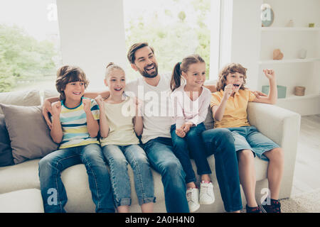 Photo of young father with youngster, youth funky kids big toothy smile, raised hands up sit on comfort, cozy sofa in bright lovely living flat room a Stock Photo