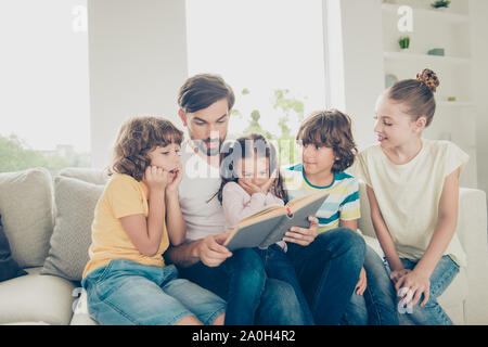 It seems we have not heard this story yet! Brunet dad read book for four  kids in casual wear