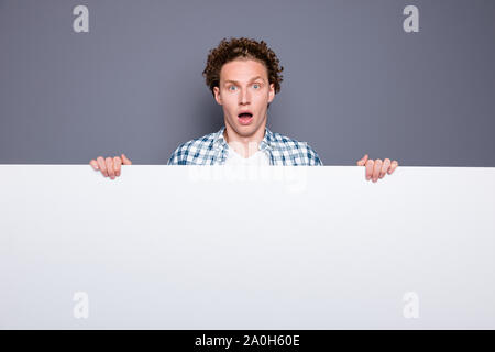 Stylish trendy attractive nice handsome shocked astonished funny positive young man with wavy hair in casual checkered shirt, holding white promo boar Stock Photo