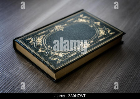 Antique book with green cover with golden decorations resting on the wooden table Stock Photo