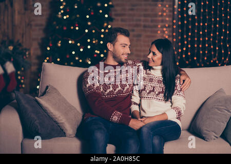 Profile side view photo of two persons in jeans, ornament sweater sit in living room couch with illumination garland decorations on pine three backgro Stock Photo