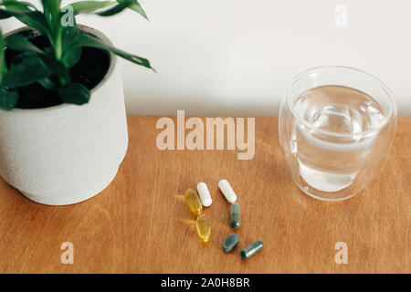 Dietary supplements. Omega 3, spirulina, chlorophyll,magnesium  capsules and glass of water on wooden table. Morning vitamin pills. Health support and Stock Photo