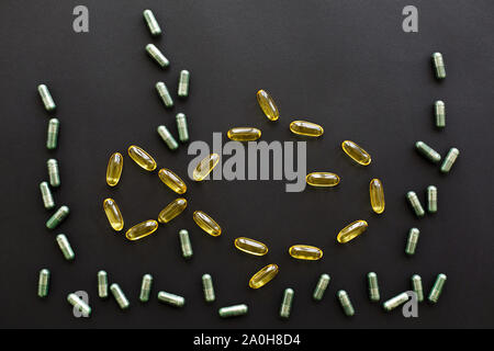 Dietary supplements. Omega 3 capsules in fish shape and spirulina pills as algae seaweed on black dark background. Flat lay. Health support and treatm Stock Photo