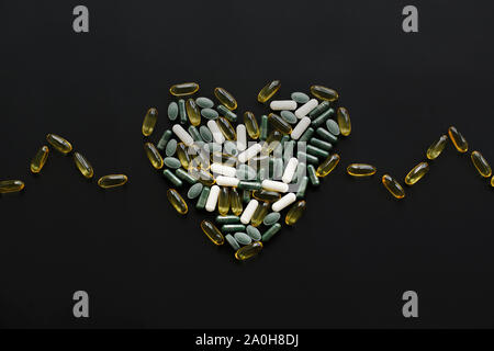 Health support concept. Omega 3, spirulina, chlorophyll, magnesium capsules in heart shape on black dark background. Dietary supplements. Heart made o