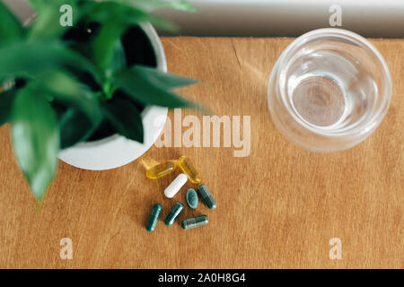 Dietary supplements. Omega 3, spirulina, chlorophyll,magnesium  capsules and glass of water on wooden table. Morning vitamin pills. Health support and Stock Photo