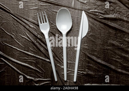 Plastic cutlery, forks, spoons and knives. Pollution of the environment with plastic and microplastics. Black plastic background. Stock Photo
