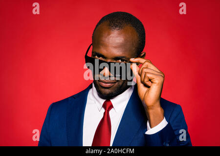 Close up portrait of handsome man in style jacket suit looks over spectacles on camera stand isolated on red bright background Stock Photo