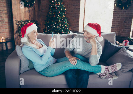 Mature elderly friend. Cheerful glad funny positive sweet lovely grey-haired married spouses granny sitting on couch divan sofa in house taking making Stock Photo