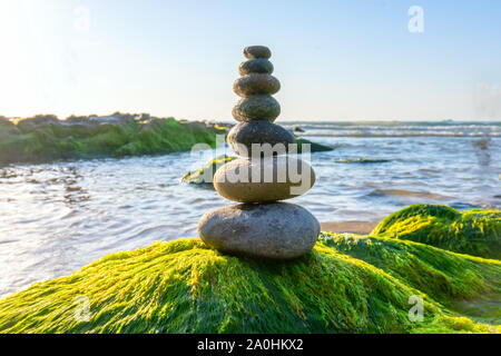 Stacked Pebbles art on mossy rocks welcomes beautiful new day Stock Photo