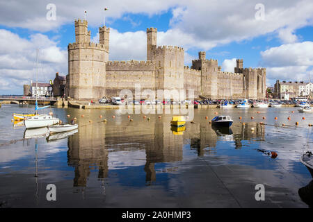 View of Edward 1st 13th century castle reflected in Afon Seiont River at high tide with moored boats. Caernarfon, Gwynedd, Wales, UK, Britain Stock Photo