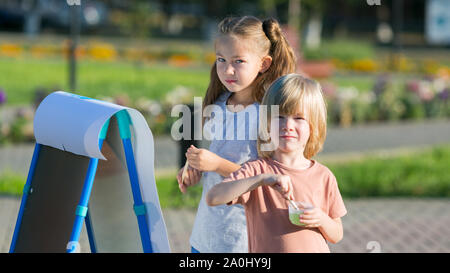 Girl with a younger brother draw paints on paper city park Stock Photo