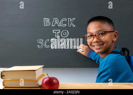 Back to school. Boy writes on blackboard with text 'BACK TO SCHOOL'. Stock Photo