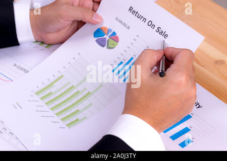 Close-up of businessman hand holding a paper document of financial report of Return on Investment, ROI. Analysing on investment risk management. Busin Stock Photo