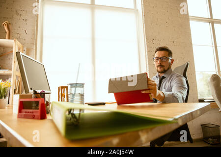 Deals. A young businessman working in the office, getting new work place. Young male office worker while managing after promotion. Looks serious, confident. Business, lifestyle, new life concept. Stock Photo