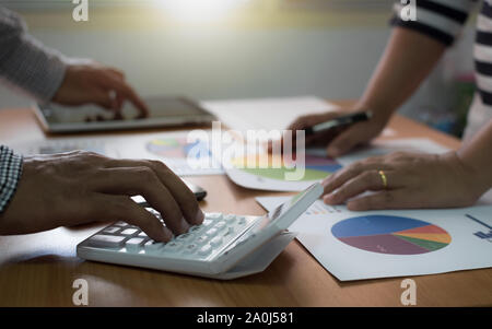 Two colleagues discussing data with calculator and tablet with marketing information graph on desk. Business team analyzing and strategy concept. Stock Photo