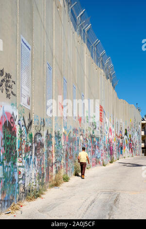 Palestine, West Bank, Bethlehem. A Palestinian man walks past a portion of the Israeli West Bank Barrier wall covered in graffiti. Stock Photo