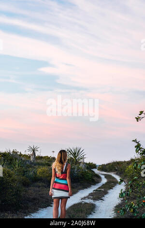 Back view of woman wearing stylish dress on path in the beach at dusk