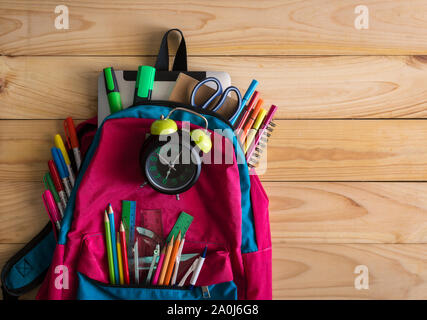 School backpack with school supplies and clock on wooden table background. Back to school concept. Stock Photo