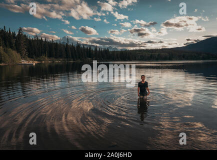 Teenage boy standing in a lake in the Rocky Mountains at sunset. Stock Photo