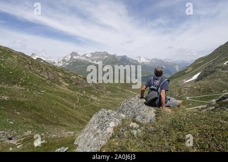 A man sitting on a rock face appreciating the alpine scenery. Stock Photo