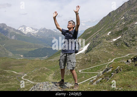 A middle aged man raises his arms in thankful gesture on a mountain, Stock Photo