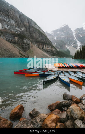 Colorful canoes at dock on Moraine Lake with mountains in background. Stock Photo