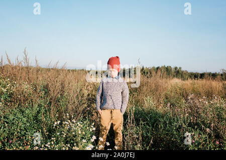 young boy stood in a field with his hands in his pockets thinking Stock Photo