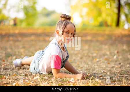 A front portrait of a little girl lying on a colorful leaves in autumn park Stock Photo