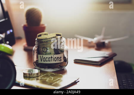 Vacation budget concept. Money for vacations savings in a glass jar with compass, passport, clock, credit card, aircraft toy and world map on working Stock Photo
